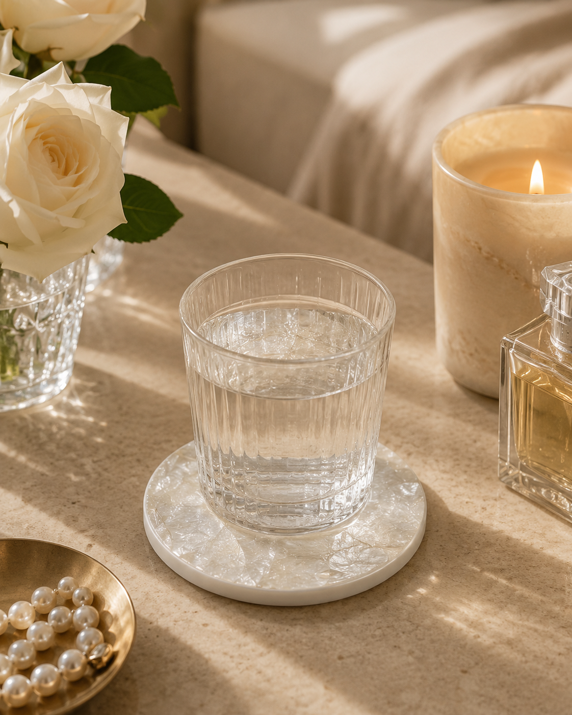 Clear glass of water on a golden mother of pearl coaster with a candle and flowers in the background