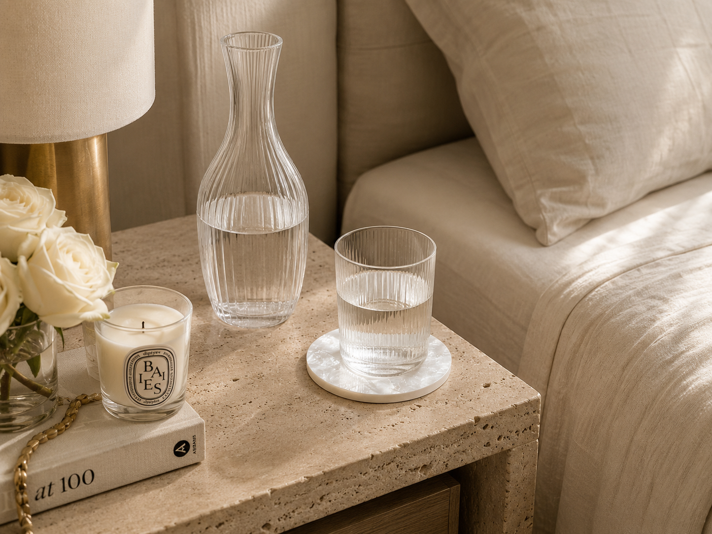 Mother of pearl coaster on nightstand including a candle, carafe, glass, and flowers.