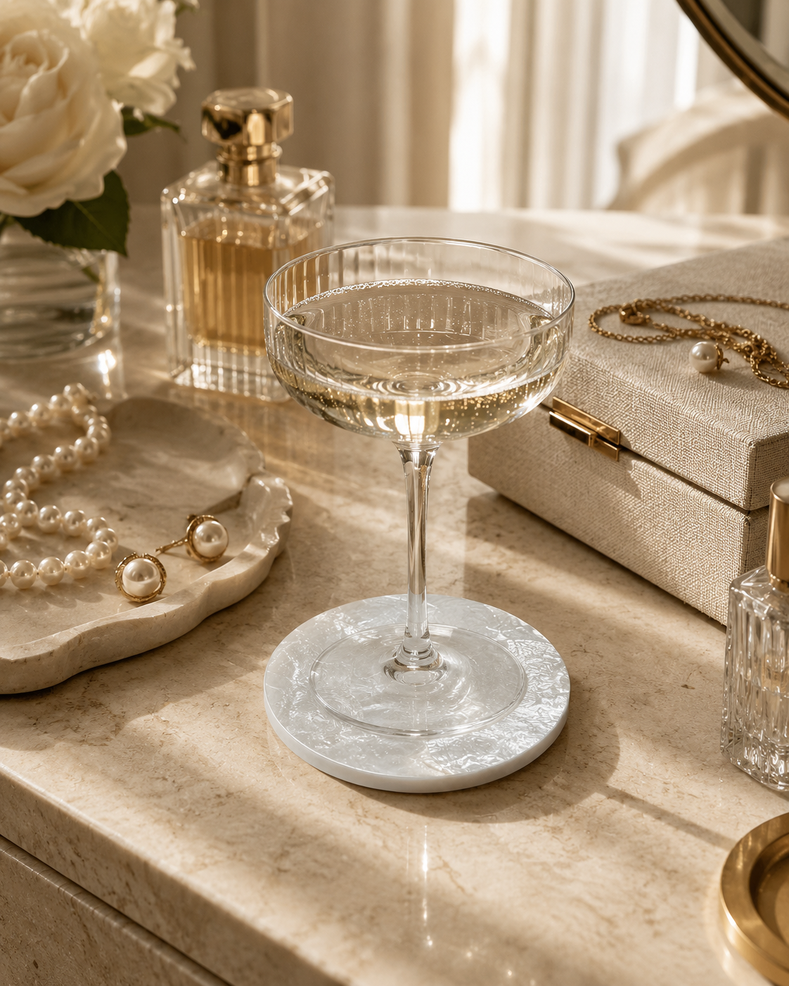 Cocktail glass on a mother of pearl coaster with jewelry and perfume bottles in the background